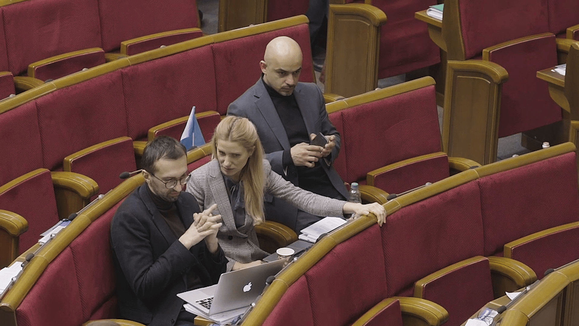 tři lidé sedí na sedačkách v sále